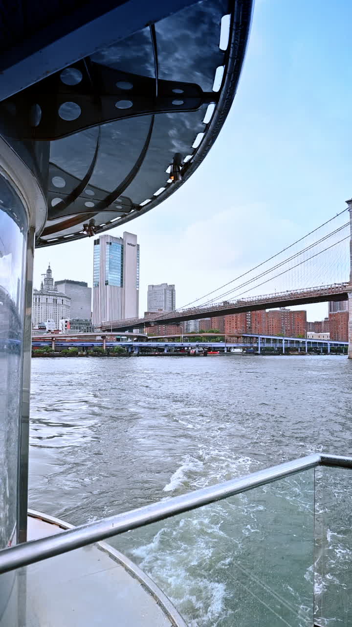 Sunny water views in NYC. A boat glides through the East River, showcasing Brooklyn Bridge and Manhattan's skyline under clear skies
