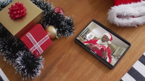 Smiling-african-american-man-wearing-santa-costume-on-christmas-video-call-on-tablet