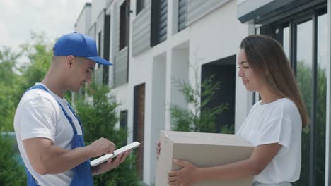 beautiful woman meets a delivery man who gives her a parcel box beside her home, courier checks information on tablet. home delivery, online shopping