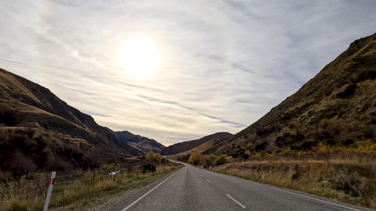 A serene drive through New Zealand's mountainous terrain during autumn, showcasing winding roads, vibrant foliage, and a bright sunlit sky