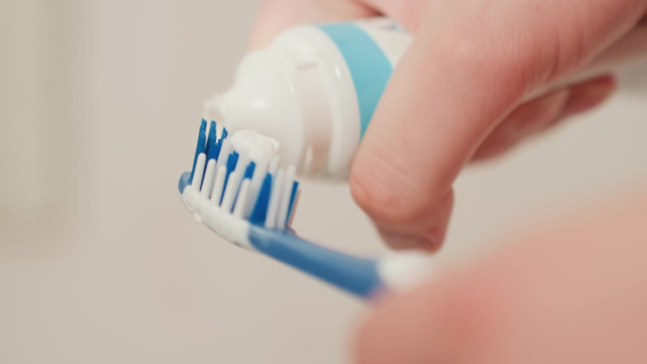 Close-up of Hand Squeezing Toothpaste onto a Toothbrush