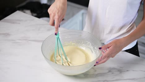 mujer irreconocible mezclando ingredientes en el cuenco usando batidor. cocina casera. disparo en cámara lenta
