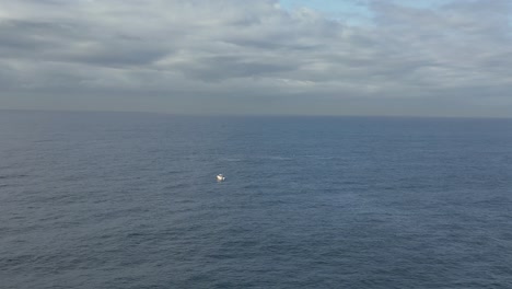 Humpback-whale-breaches-in-the-distance-next-to-a-fishing-boat-on-the-ocean