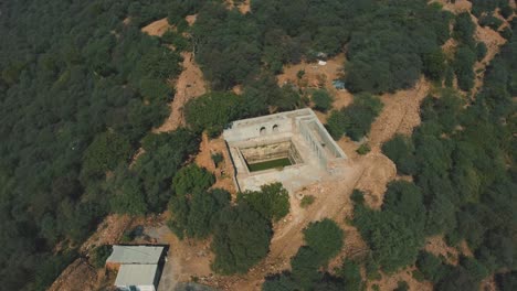 Aerial-drone-shot-of-an-ancient-tank-or-kund-on-a-top-of-a-hill-fort-surrounded-by-forest-in-Gwalior-,-India