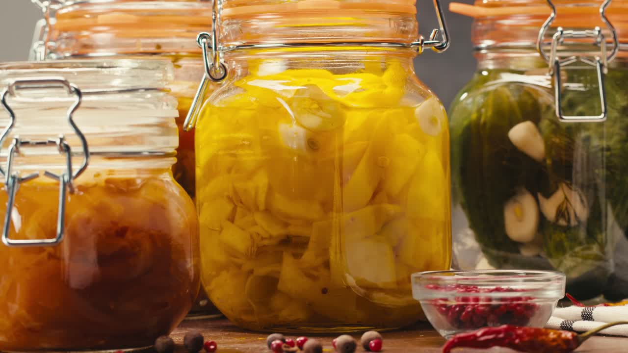 Fermented food in glass cans on table close-up. Preservation of vegetables in glass jars. Fermentation preserved mini corns, kimchi, cucumbers, mushrooms with spices.