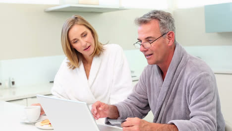 Mature-smiling-couple-shopping-online-at-breakfast