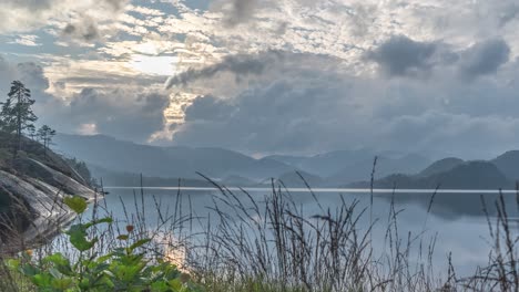 Wirbelnde-Wolken-Werden-Von-Der-Untergehenden-Sonne-Von-Hinten-Beleuchtet-Und-Auf-Der-Spiegelähnlichen-Oberfläche-Des-Sees-Reflektiert