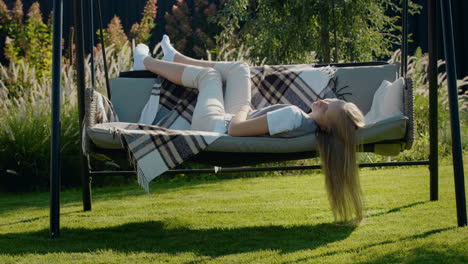 una chica de cabello largo se acuesta en un columpio de jardín, se relaja en un caluroso día de verano