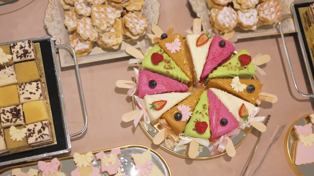 Ovenfra-billede af en farverig dekoreret kage med skiver arrangeret i et cirkulært mønster, sammen med assorterede kager og søde sager.