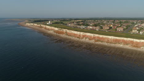 toma aérea de alto establecimiento de los antiguos acantilados estratificados de bandas blancas y naranjas de hunstanton con el faro y el naufragio del barco de arrastre de vapor sheraton al atardecer en el norte de norfolk, reino unido