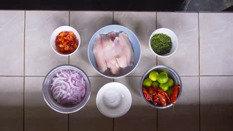 On-a-table,-there's-a-dish-with-layered-chicken,-onions,-peppers,-mint-leaves,-and-lime-wedges