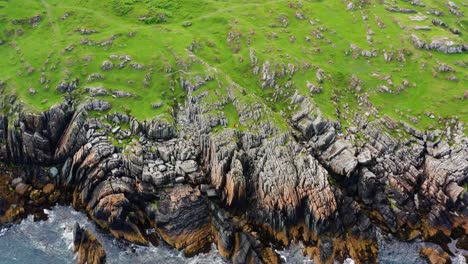 aerial orbit over clogherhead cliffs with people relaxing beside rugged greywacke and mudstone rocks on an overcast day