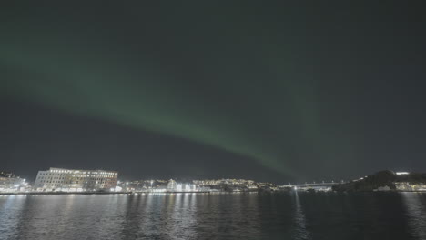 timelapse of moving green northern light aurora borealis above the city kristiansund norway on a clear night with water in the front and part of the city in the background log