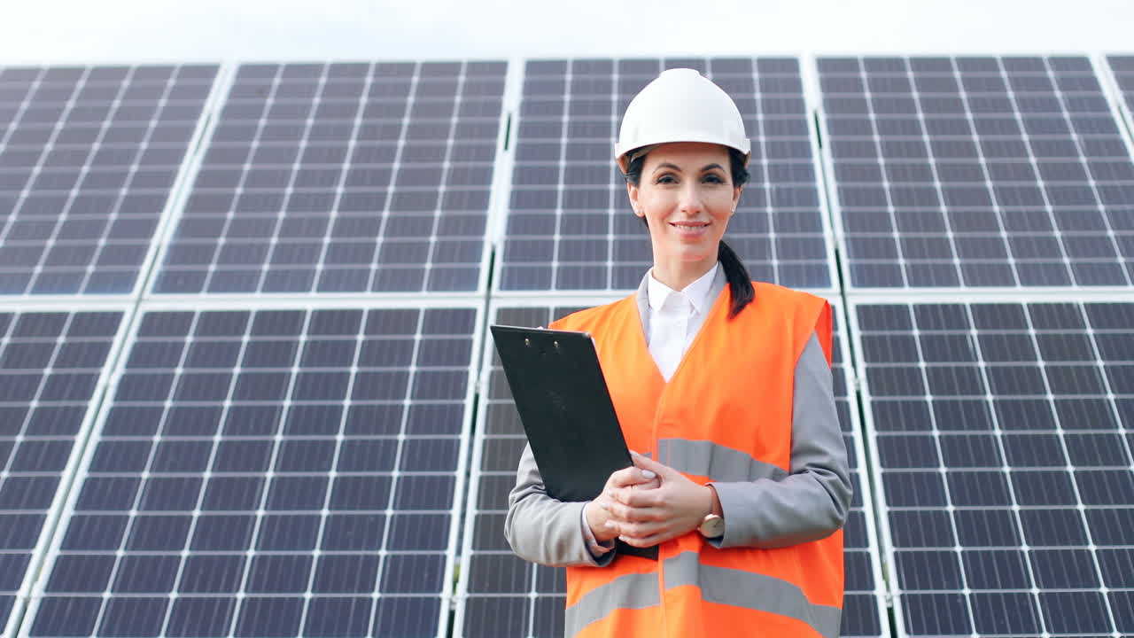 retrato de una joven ingeniera con uniforme especial y casco sosteniendo un portapapeles cerca de paneles solares