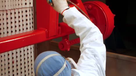 Female-worker-pulverizing-red-paint-on-industrial-unit-in-workshop