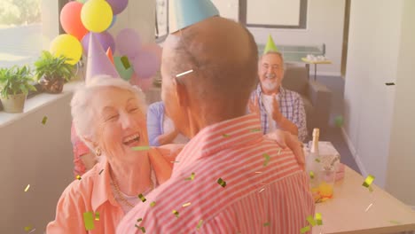 Golden-confetti-falling-against-caucasian-senior-couple-dancing-together-during-birthday-party