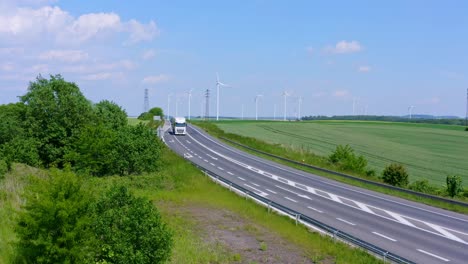 white truck driving on a country road with huge ecological wind farm in background