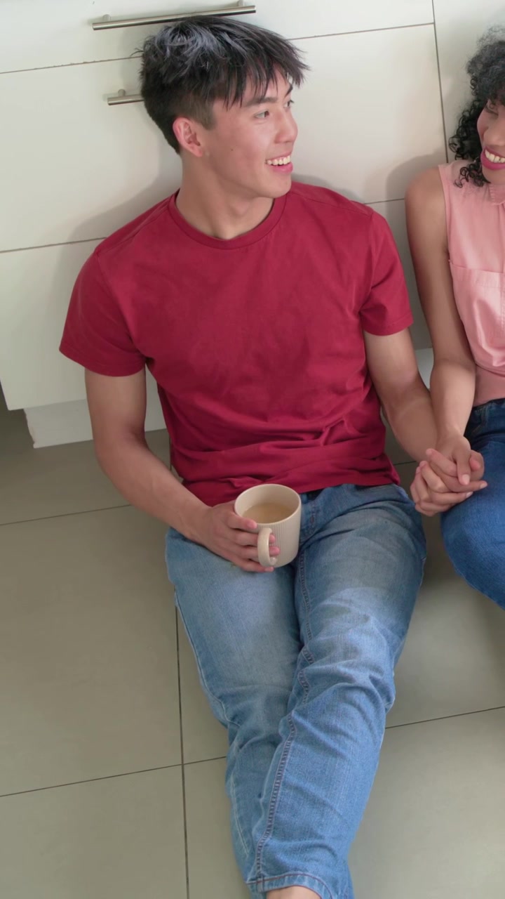 Couple sitting kitchen floor holding hands, man raising mug starting motion clink graphic for ads