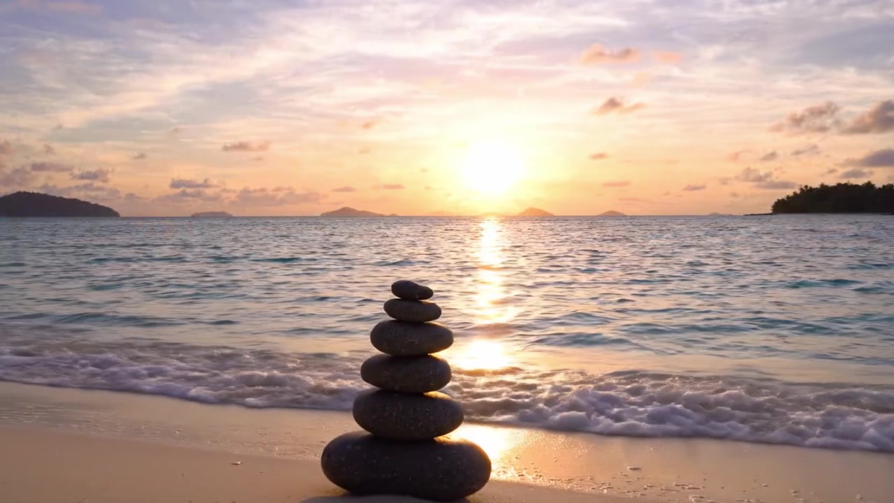 Coucher de Soleil Serein sur la Plage avec une Pile de Pierres Équilibrée au Milieu d'un Paysage Tropical et de Douces Vagues Reflétant une Lumière Douce du Soleil
