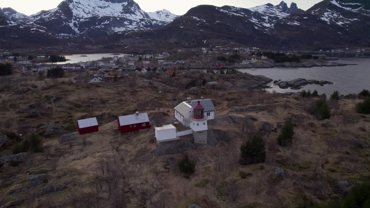 fotografía aérea de un faro histórico con el famoso pueblo de sorvagen en el fondo y las montañas cubiertas de nieve