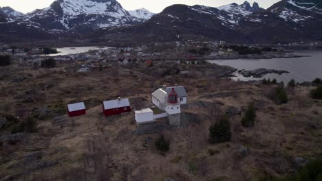 Aerial-forwarding-shot-of-a-historical-lighthouse-with-the-famous-village-Sorvagen-in-the-background-and-snow-covered-mountains