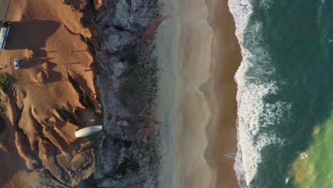 aerial drone bird's eye top view following a paraglider flying over the cliffs of cacimbinhas in pipa, brazil rio grande do norte as small waves crash into the beach on a warm summer day