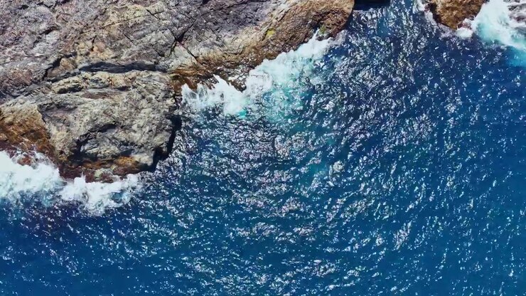 Le onde si infrangono contro la costa rocciosa mentre l'acqua blu riempie la vista sull'oceano durante le ore diurne