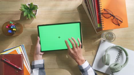 vista de arriba hacia abajo de una computadora portátil con pantalla verde simulada pantalla chromakey en un escritorio de oficina de madera al lado de la libreta con bolígrafos, gafas y un vaso de agua.