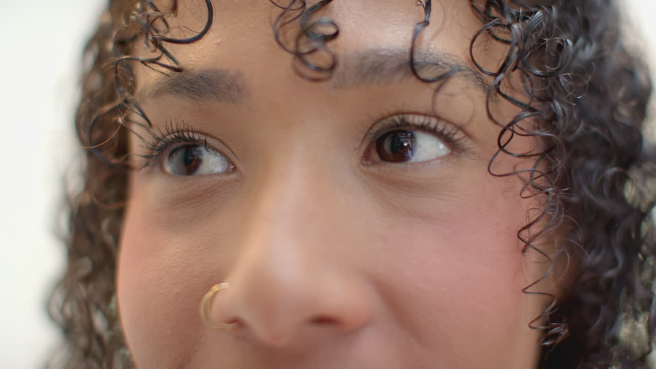 Close-up of woman with curly hair and nose ring, looking thoughtfully