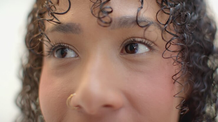 Close-up wanita berambut keriting dan tindik hidung, terlihat berpikir