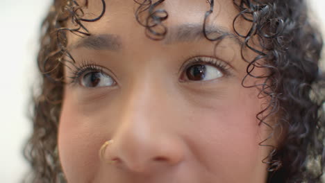 close-up of woman with curly hair and nose ring, looking thoughtfully