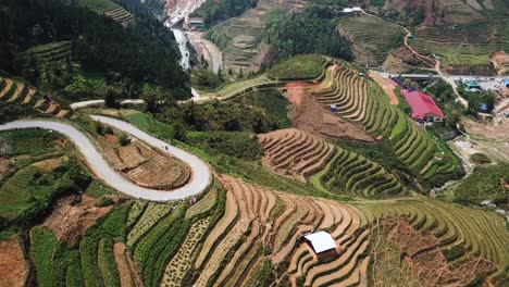 una toma aérea mira hacia los campos en terrazas y muestra una motocicleta subiendo por un camino sinuoso