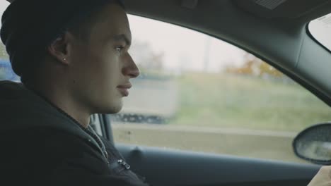 happy young man in a car turns his head to the side smiling at camera while driving - closeup, handheld