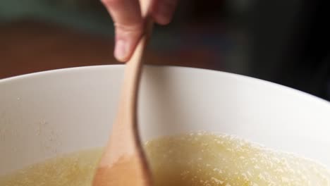 macro shot of hand mixing delicious food in bowl with wooden spatula