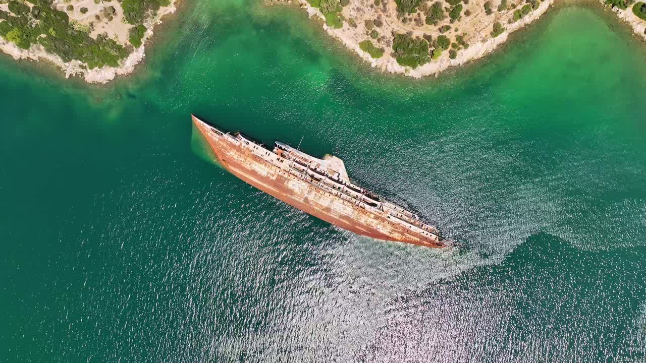 Dynamic drone pan capturing the sunlit wreck of the Mediterranean Sky in Piraeus under bright blue Greek skies.