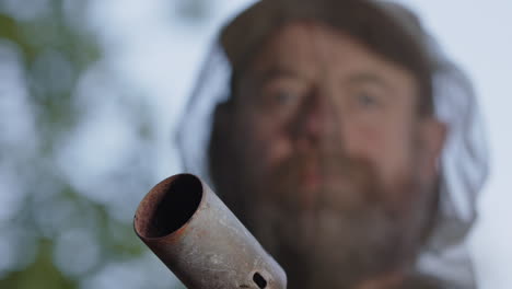 man lights blowtorch with lighter in front of face wearing mosquito head net