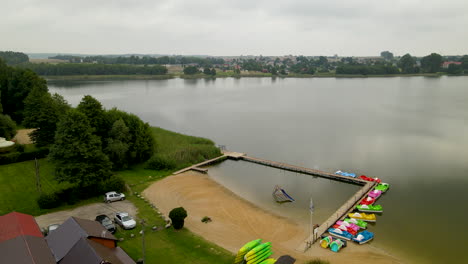 antena - lago hartowiec con embarcadero de madera vacío con playa de arena y botes estacionados y tablas de pedales cerca del muelle durante el día