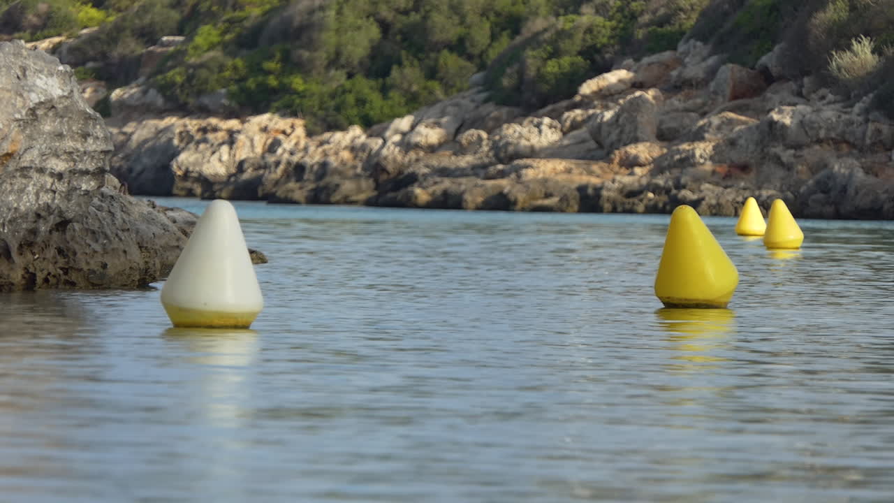 날카로운 바위와 녹색 초목이 있는 작은 만에 있는 보트의 채널을 나타내는 노란색 원추형 탐색 부표
