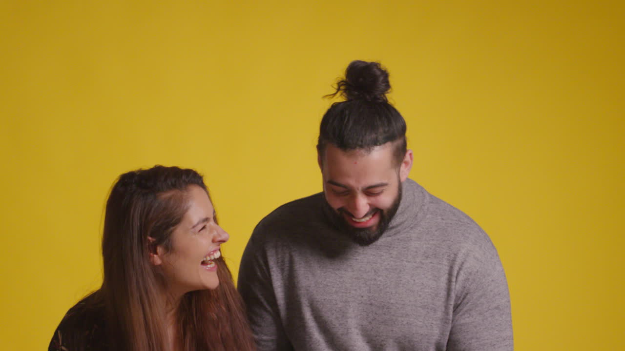 Scatto in studio di una coppia entusiasta che festeggia la vincita di un premio in denaro, lanciando una manciata di banconote da 100 dollari in aria su sfondo giallo
