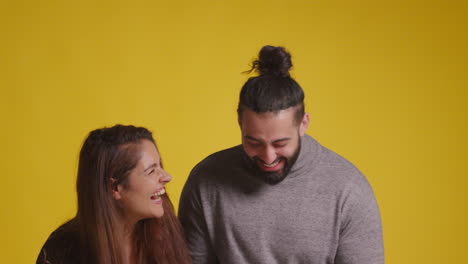 studio shot of excited couple celebrating winning cash prize throwing handful of 100 dollar bills in the air against yellow background