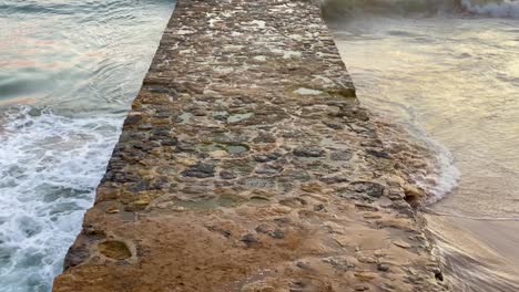 Primer-Plano-De-La-Entrada-Al-Pontón-Del-Océano-Con-Una-Gran-Puesta-De-Sol-En-El-Fondo-En-La-Playa-De-Cascais-Con-Algunas-Olas-Rompiendo