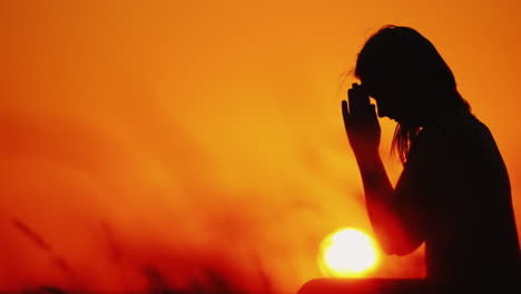 Silueta-De-Una-Mujer-Rezando-En-El-Contexto-De-Un-Cielo-Naranja-Y-Un-Gran-Sol-Poniente