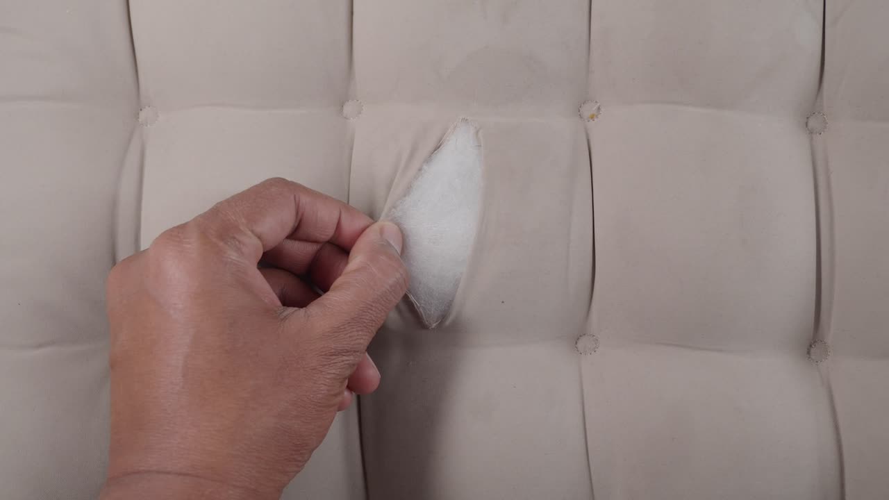 Mano che strappa un tessuto danneggiato su un cuscino beige