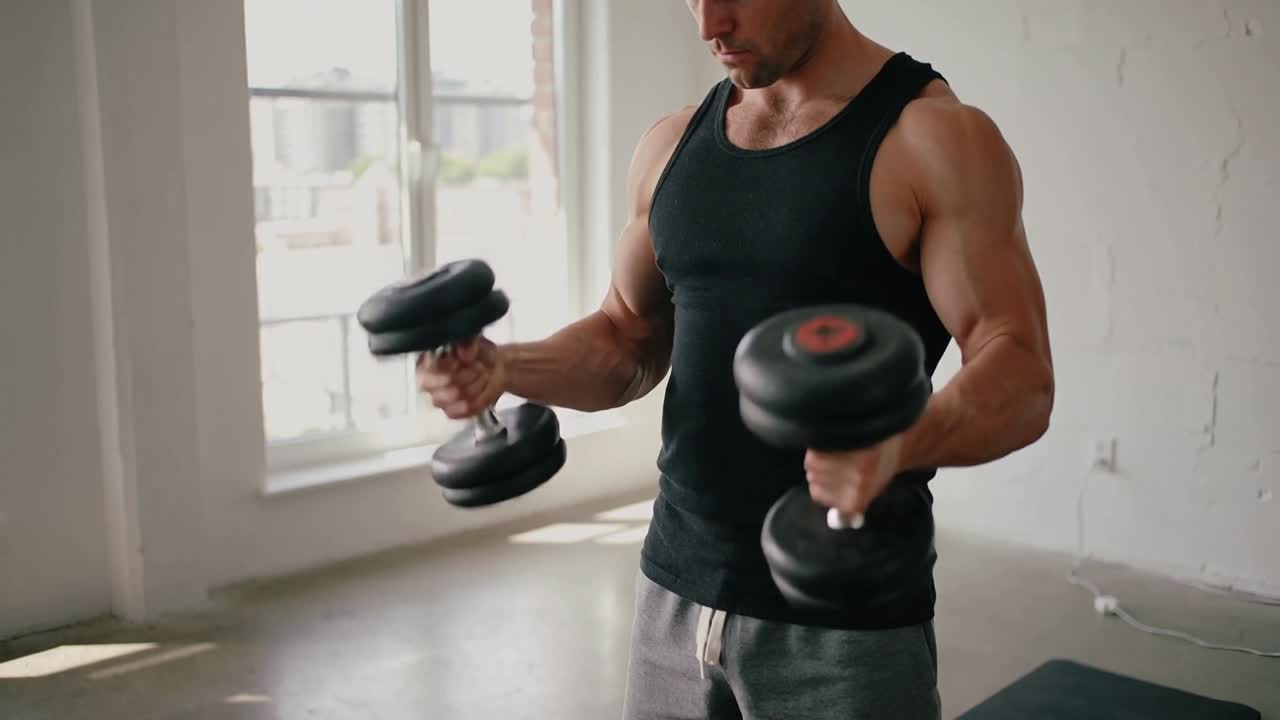 Preparing to lift, man in black tank curling adjustable dumbbells at home gym for strength