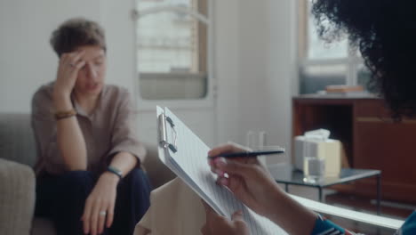psychologist writing down notes on clipboard during therapy session