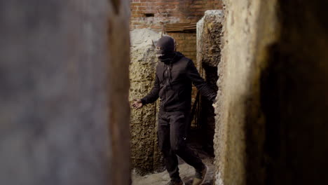 masked man wearing black clothes holding an ax while walking in a ruined building