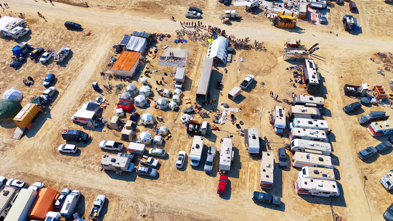 Overhead view of dense desert camp. A packed cluster of tents, RVs and bikes fills the sandy festival camp grid