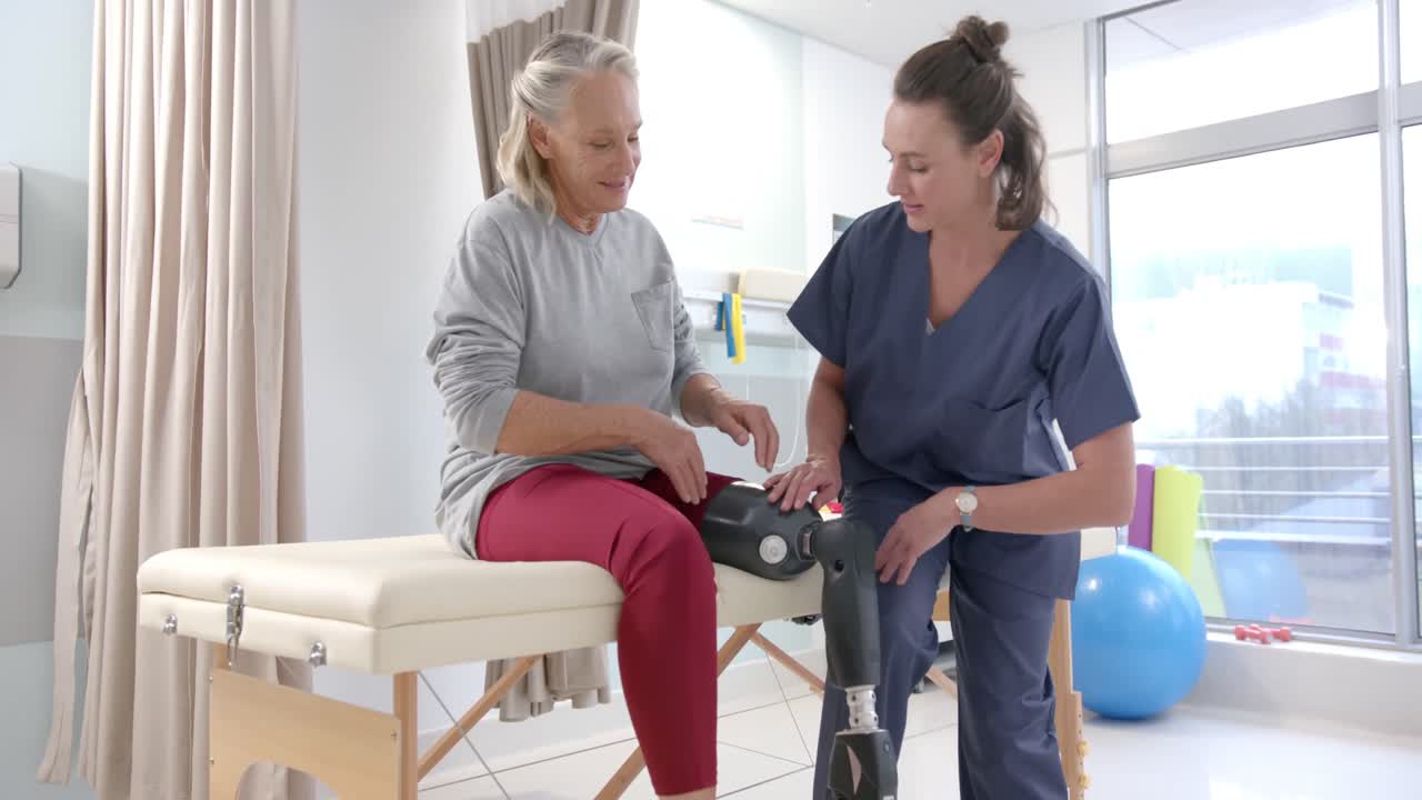 Caucasian female physiotherapist stretching prosthetic leg of female patient at rehab center