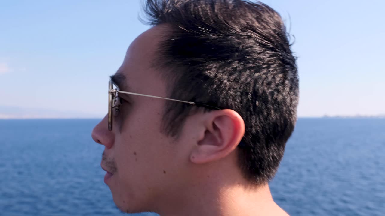 Slow Motion Intimate Close Up of Young Vietnamese Man with Aviator Sunglasses Surrounded by Blue Water