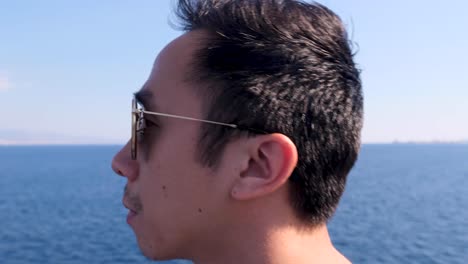 slow motion intimate close up of young vietnamese man with aviator sunglasses surrounded by blue water